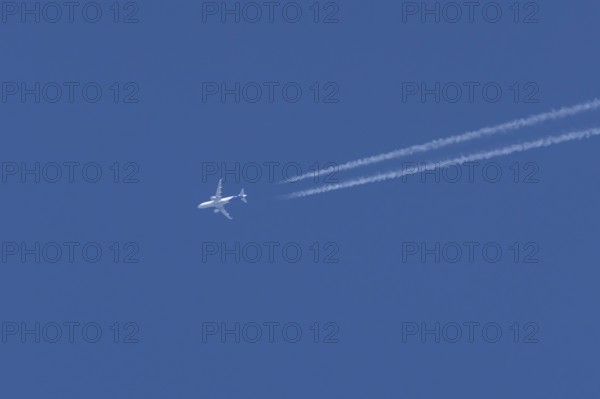 Airbus jet passenger aircraft flying in a blue sky with contrails or vapour trails behind, England, United Kingdom
