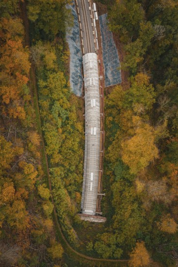Aerial view of a partly covered railway tunnel surrounded by colorful trees, Hermann-Hesse-Bahn construction site, Calw, Germany