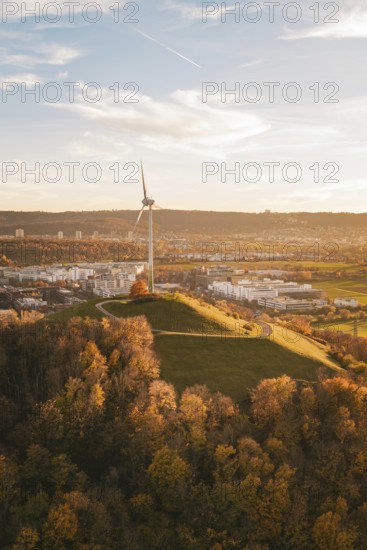 A wind turbine on a hill surrounded by autumn trees and urban landscape, Grüner Heiner, Korntal, Germany