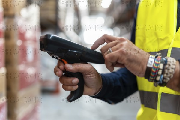 Warehouse worker in high visibility vest holding a barcode scanner, efficiently managing inventory and tracking products for logistics and supply chain operations