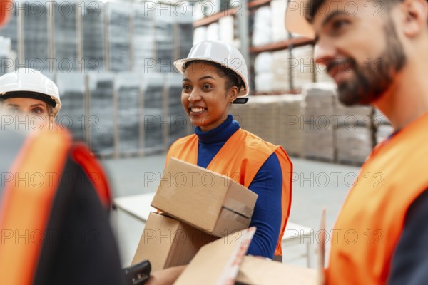 Diverse team of logistics workers wearing safety vests and hard hats, collaborating on picking and packing cardboard boxes in a busy distribution warehouse