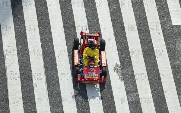 People in costumes drive small go-kart racing cars across zebra crossings, Shibuya Crossing, Shibuya, Tokyo