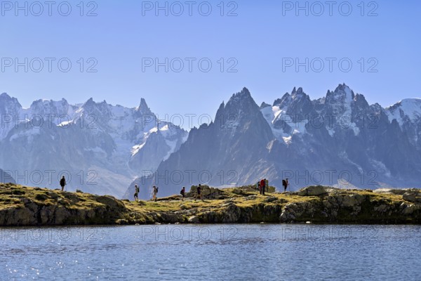 A group of hikers at Lac de Chésserys, behind the snow-covered Mont Blanc massif, Chamonix-Mont-Blanc, Haute-Savoie, France
