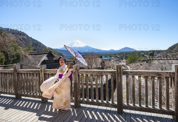 Japanese woman in kimono with umbrella, Iyashinosato open-air museum, old Japanese village with traditional houses, at the back volcano Mt. Fuji, Fujikawaguchiko, Saiko, Japón