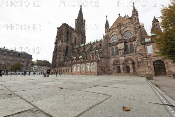 Strasbourg Cathedral impresses with its Gothic architecture. Passers-by moves around the square while the trees start to lose their leaves in autumn. Bas Rhin, Alsace, France