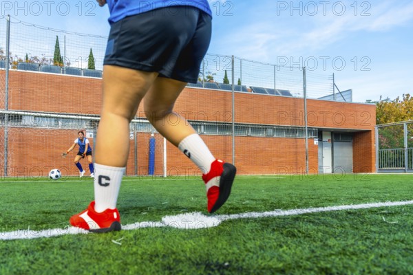Football player preparing to shoot a penalty kick on an artificial turf field, with the opposing team's goalkeeper ready to defend the goal in the background
