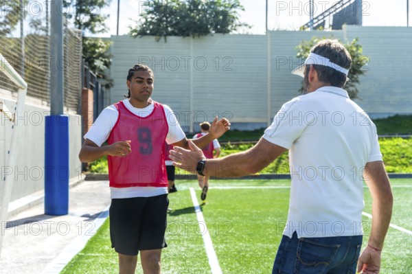 Soccer coach extends a hand to a young male player wearing a number 9 bib on a green artificial turf field, symbolizing teamwork, guidance, and active sports mentorship during youth training