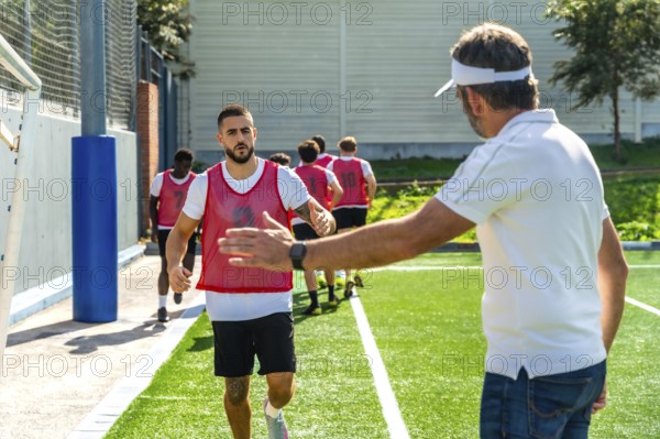 Soccer team players running sprints on a green artificial turf field, receiving an encouraging high five from their coach during a morning training session