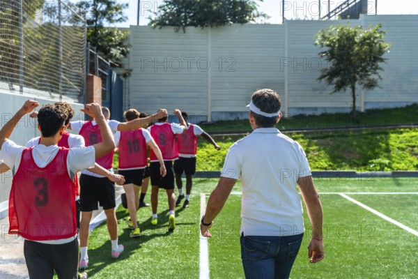 Youth soccer coach leading a group of players in red training vests across artificial grass, preparing the team for practice with guidance, teamwork and focus