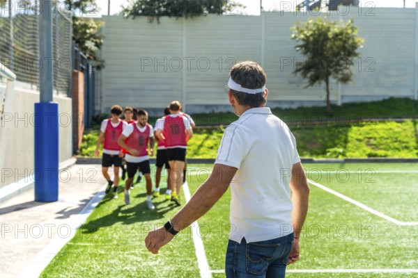 Soccer coach watches youth team warming up on artificial turf, guiding drills and preparation for training session with focus on teamwork, skill building and fitness