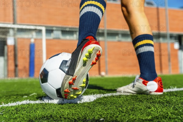 Female soccer player wearing a cleat and blue socks standing with a ball on a green artificial turf field, preparing to play a competitive game with focus