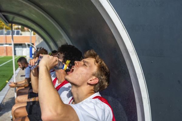Soccer teammates on the bench rehydrating with bottled water during a break in training or a match, resting and regaining energy after intense physical effort