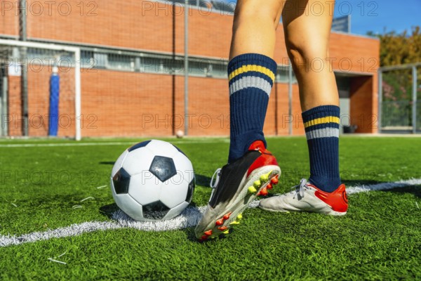 Female soccer player's legs and feet are positioned near a soccer ball on a green artificial turf field with white lines, featuring athletic performance and preparation