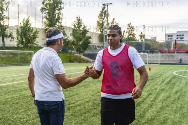 Soccer coach and young player shaking hands on an artificial turf field, demonstrating teamwork, sportsmanship, and mentorship during a training session