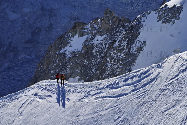 Two ascended mountaineers run across a snow-covered mountain ridge, Aiguille du Midi, Chamonix-Mont-Blanc, Haute-Savoie, France