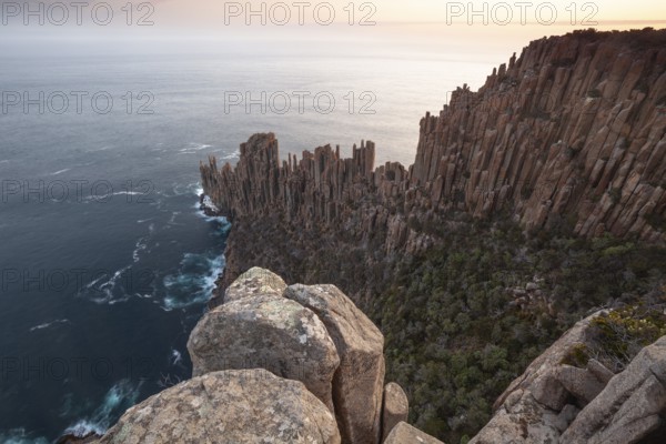 Long exposure shows sunset over the cliffs of Cape Raoul. Golden light hits the sea and colors the rocks warmly in the evening. Cape Raoul, Tasman Peninsula, Tasmania, Australia