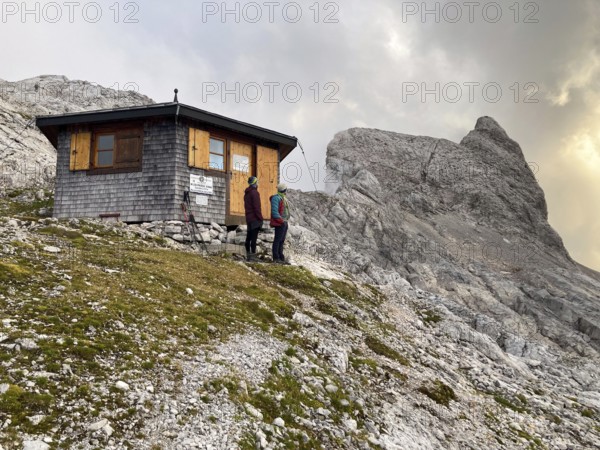 Two mountaineers in front of the Wildalmkirchl bivouac, in the background the summit of Wildalmkirchl, Steinernes Meer, Berchtesgaden Alps, Austria