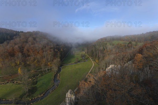 Autumn landscape with rising fog over the Grosse Lauter river loop in Lautertal at sunrise. View from above of the picturesque valley with colorful deciduous forest and rolling hills, Großes Lautertal, Baden-Württemberg, Germany