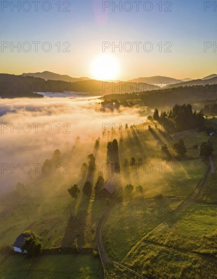 Sunrise over a fog covered village in a rural landscape, golden morning light, serene autumn atmosphere, hills and mountains in the background, AI generated