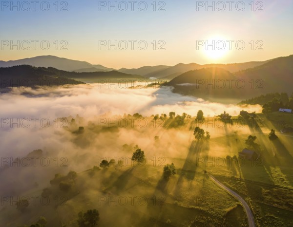 Sunrise over a fog covered village in a rural landscape, golden morning light, serene autumn atmosphere, hills and mountains in the background, AI generated