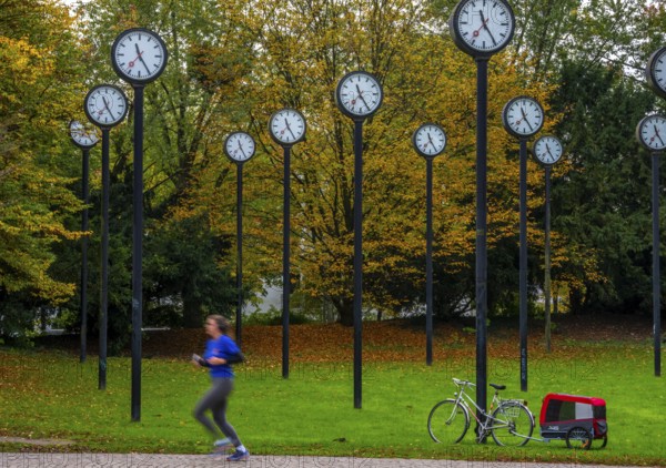 The art installation Zeitfeld in Volksgarten Park in Düsseldorf-Oberbilk, a total of 24 station clocks, on 6 meter high steel columns, have been running synchronously since 1987, jogger in the municipal park, artwork by Düsseldorf artist Klaus Rinke, symbol of time, time change, North Rhine-Westphalia, Germany
