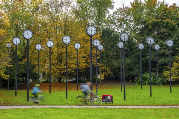 The art installation Zeitfeld in Volksgarten Park in Düsseldorf-Oberbilk, a total of 24 station clocks, on 6 meter high steel columns, have been running synchronously since 1987, cyclists in the municipal park, artwork by Düsseldorf artist Klaus Rinke, symbol of time, time change, North Rhine-Westphalia, Germany
