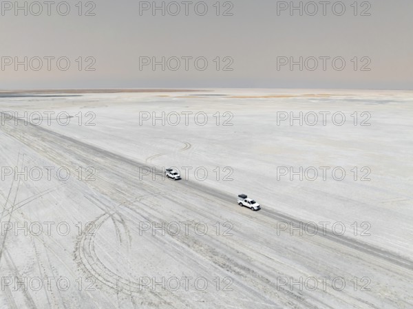 Aerial view, two off-road cars driving on a salt pan, arid landscape, Botswana