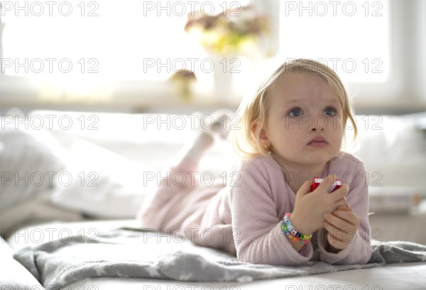 Child, girl, 4 years, blonde, lying on sofa, watching TV, watching television, watching television, excited, Stuttgart, Baden-Württemberg, Germany