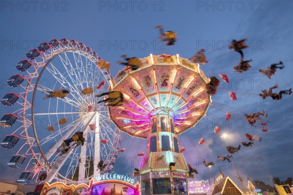 An illuminated chain carousel and Ferris wheel at night at a funfair, people swinging on chains, Bad Cannstatt, Stuttgart, Baden-Württemberg, Germany