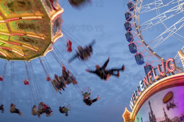 An illuminated chain carousel turns at night at a funfair, with floating people and colourful lights, Bad Cannstatt, Stuttgart, Baden-Württemberg, Germany