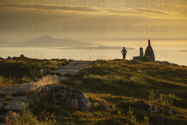 Woman standing next to cairn and looking at the sea, Rørsethornet stone staircase, with 3292 steps one of the longest continuous stone staircases in the world, Sherpat stairs or Midsund stairs or Midsundtrappene, Rørsethornet hike, evening mood, Otroya or Otrøya island, Møre og Romsdal, Norway