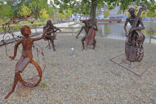 Sculpture The Concert by Günther Fahrner, rusty, metal sculpture, sheet metal, modern art, four bizarre whimsical musicians, trio, quartet, double bass player, violin player, cello player, string instruments, cello, violin, double bass, make music, musician, pond, bull figure, Bastinsweiher, Rhineland, Stolberg, North Rhine-Westphalia, Germany