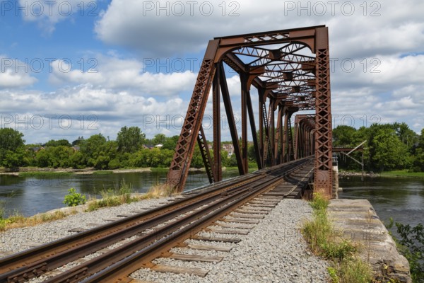 Railroad tracks leading to old rusted Terrebonne Pratt truss railroad bridge over Des Mille-Iles river in summer, Laval, Quebec, Canada