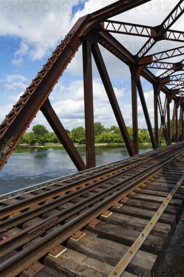 Railroad tracks leading to old rusted Terrebonne Pratt truss railroad bridge over Des Mille-Iles river in summer, Laval, Quebec, Canada