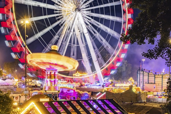 Folk festival in Stuttgart. The 178th Cannstatter Volksfest on the Wasen is one of the most important traditional festivals in Germany. Ferris wheel, chain carousel and other amusement park attractions, light effects at night. Stuttgart, Baden-Württemberg, Germany