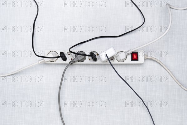 Top view of a power strip with on/off switch and various plugged-in plugs and cables on a white Resopal panel