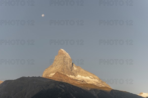 The iconic Matterhorn stands high above a clear evening sky illuminated by a bright moon. This breathtaking view captures the beauty and serenity of the Swiss Alps near Zermatt. Valais, Alps, Switzerland