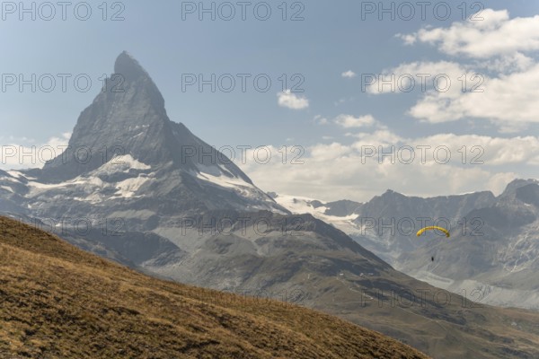 A person paraglides against the stunning backdrop of the Matterhorn mountain in Switzerland. The clear blue sky enhances the breathtaking view of the alpine landscape. Zermatt, Valais, Alps, Swiss