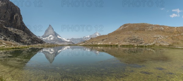 The snow-capped mountains rise majestically above a calm lake, where their towering reflections dance on the still water under a bright blue sky. Matterhorn, Zermatt, Valais, Alps, Swiss