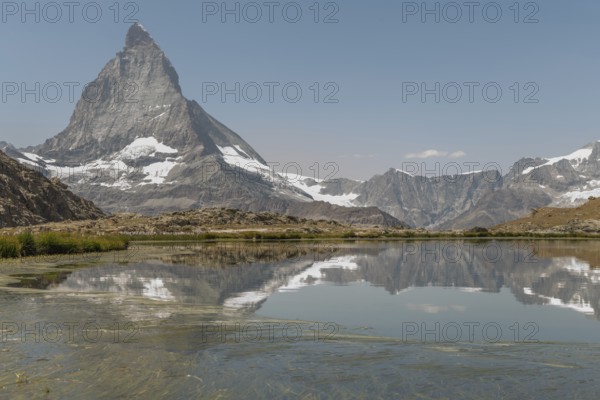 A stunning view of the Matterhorn mountain towering in the background, reflecting perfectly in a quiet alpine lake surrounded by rocky terrain and lush greenery. Zermatt, Valais, Alps, Swiss