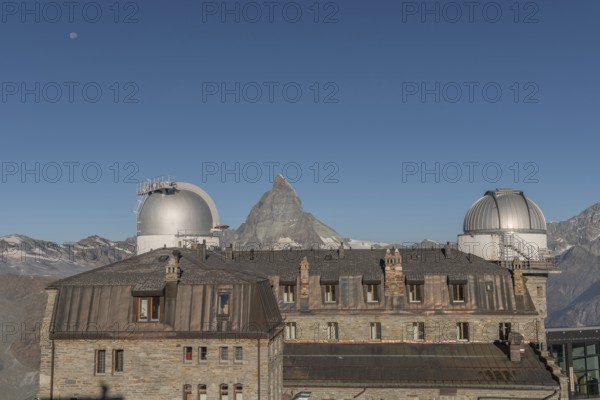 This breathtaking view shows the iconic Matterhorn mountain rising behind a historic observatory building. The clear blue sky enhances the serene atmosphere in autumn