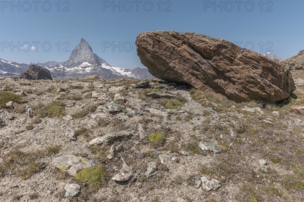 Towering Matterhorn dominates the skyline over rugged terrain and displays natural beauty. The rocky landscape offers sparse vegetation under a clear blue sky. Zermatt, Valais, Alps, Swiss