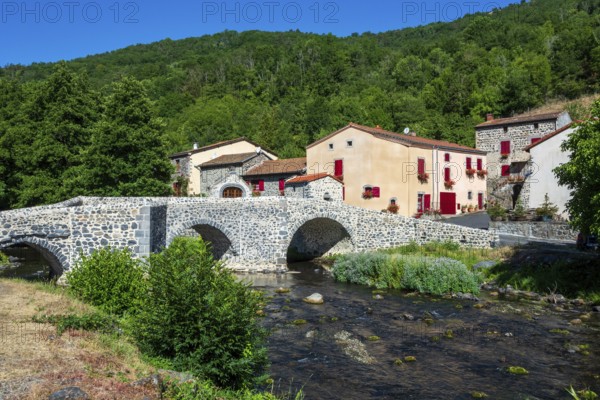 Stone bridge over the Pavin couze river flowing through the village of Saurier, Puy de Dome. Auvergne Rhone Alpes, France