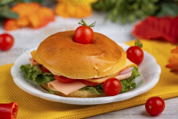 A filled bagel on a plate, decorated with tomatoes on a yellow cloth