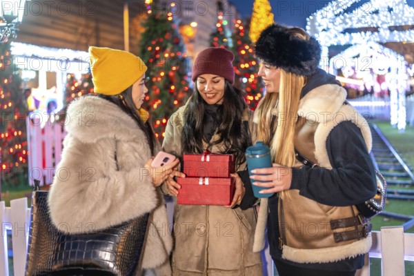 Three friends enjoying christmas time together, holding christmas gifts and a reusable cup at the christmas market