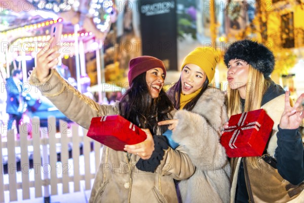 Three happy female friends are taking a selfie holding christmas gifts at a christmas market, enjoying the festive atmosphere