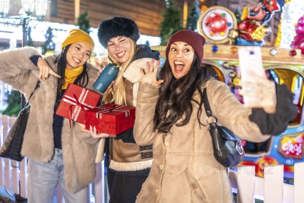 Three happy women taking a selfie at christmas market, holding presents and enjoying winter holidays