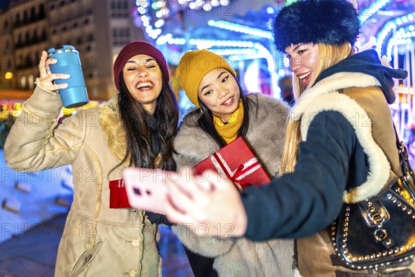 Three happy female friends are taking a selfie with a christmas gift at a christmas market, enjoying the festive atmosphere