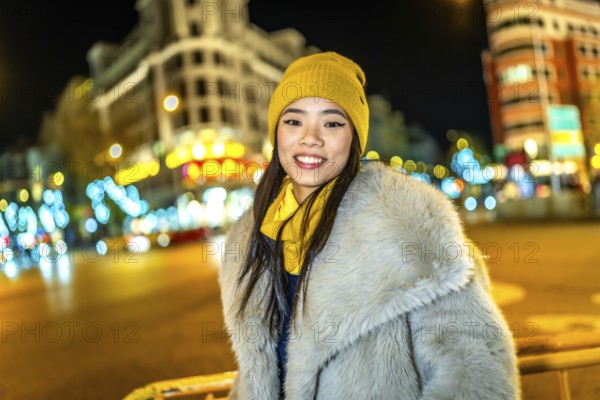 Asian woman wearing cozy winter clothes, smiling and enjoying the vibrant christmas lights illuminating the bustling city streets at night