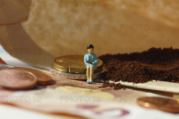 Miniature figure of a woman sitting on coins and banknotes, ground coffee in a filter bag in the background, North Rhine-Westphalia, Germany